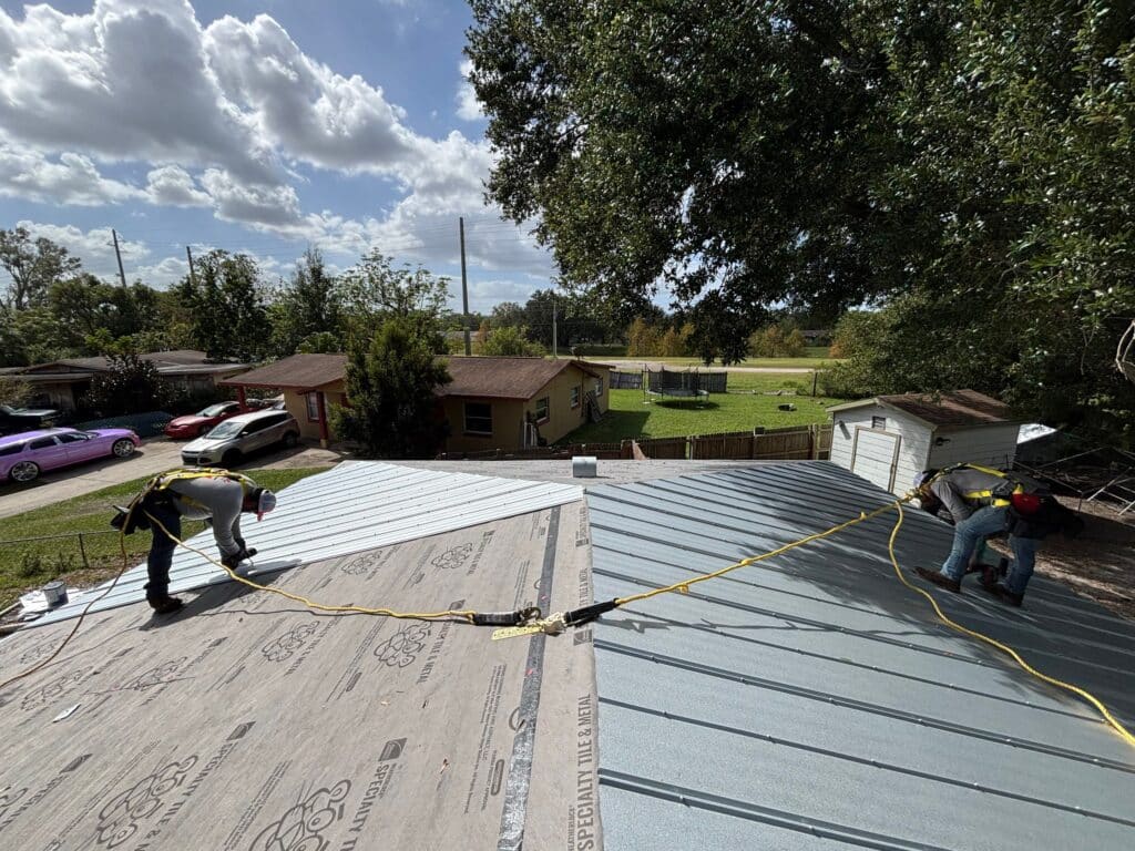 new metal roof being installed by two royalty workers with harnesses attached to middle of roof