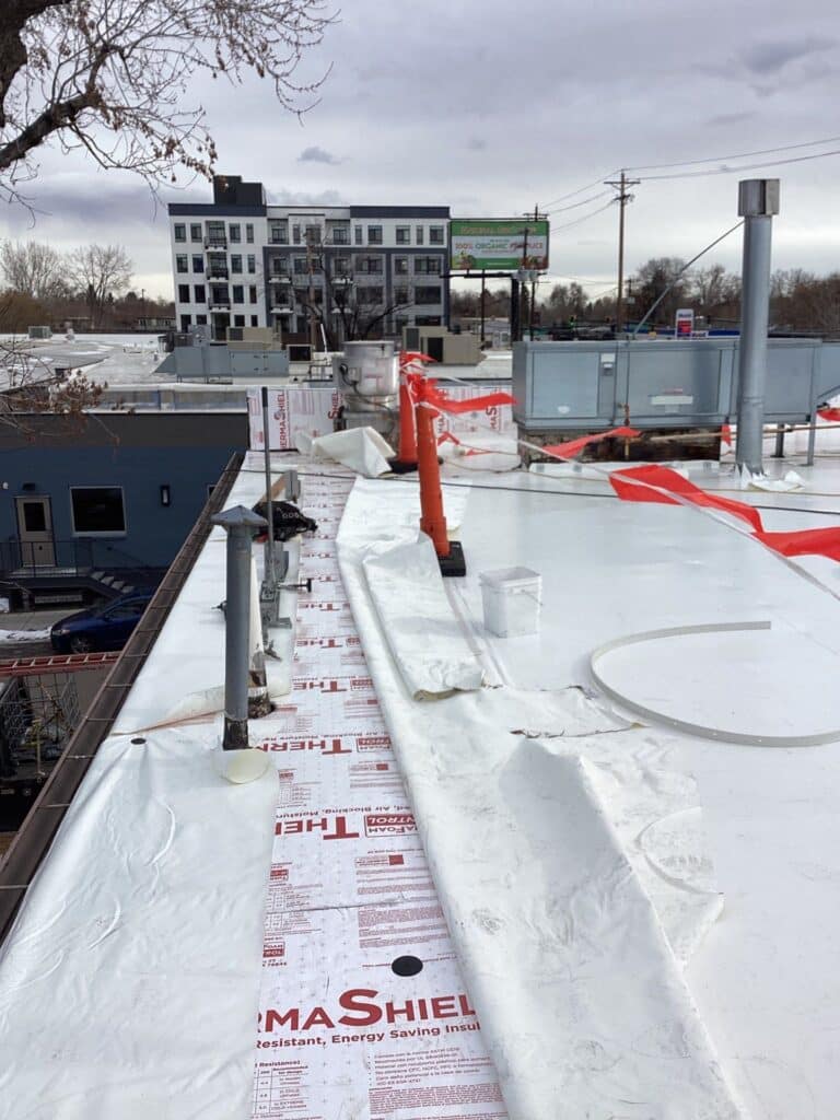 flat roof in process of replacement with safety orange flags and insulation showing as its covered by shite single-ply pvc sheets