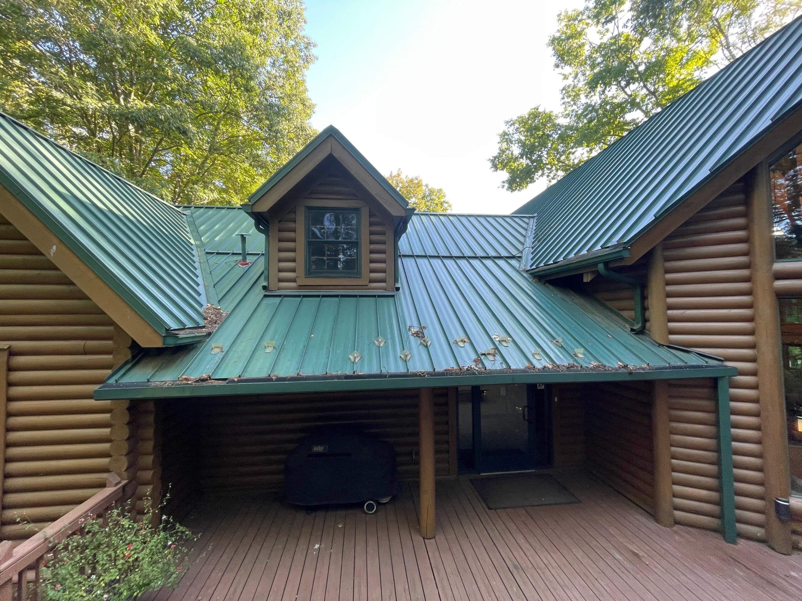 green metal roof on cabin in need of repair with leaves in gutter