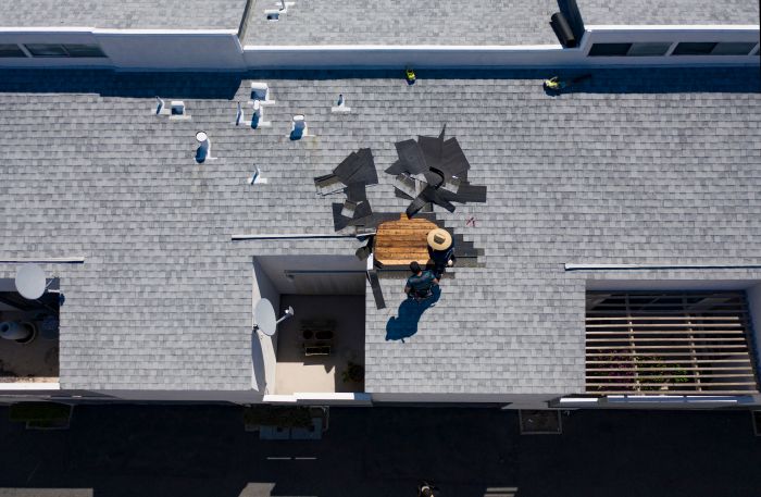 drone shot of workers looking at pile of shingles removed from a portion of a roof on home after storm damage